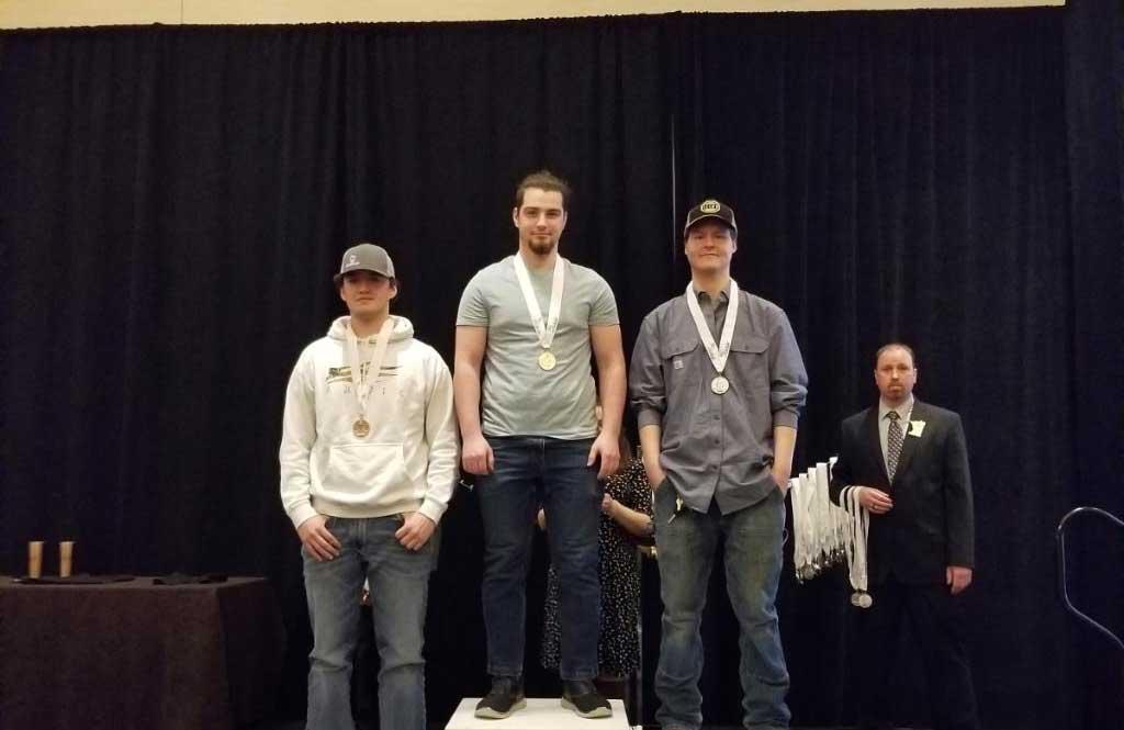 三名学生站在领奖台上，身后是一名男子颁发奖牌